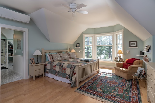 bedroom featuring a wall unit AC, wood finished floors, lofted ceiling, ceiling fan, and a wainscoted wall