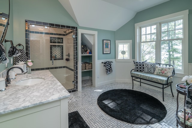 bathroom featuring plenty of natural light, a stall shower, lofted ceiling, wainscoting, and vanity