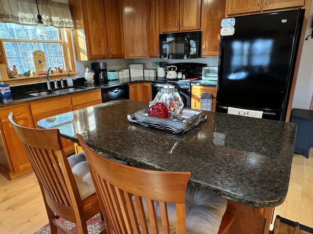 kitchen featuring black appliances, a sink, light wood-style floors, brown cabinets, and a center island
