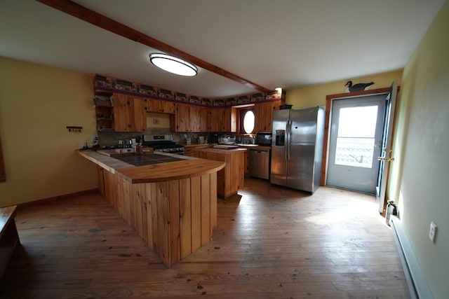 899 Golden Ridge Rd, Sherman, ME 04476 - kitchen featuring stainless steel appliances, a peninsula, a baseboard heating unit, wood-type flooring, and decorative backsplash