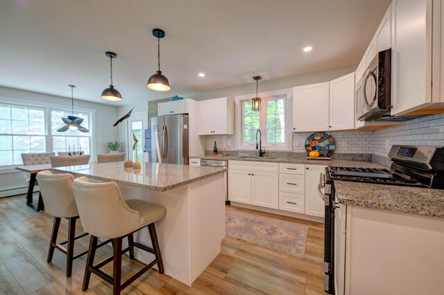 26 John Adams Ct, Naples, ME 04055 - kitchen featuring stainless steel appliances, a sink, light wood finished floors, decorative backsplash, and a center island