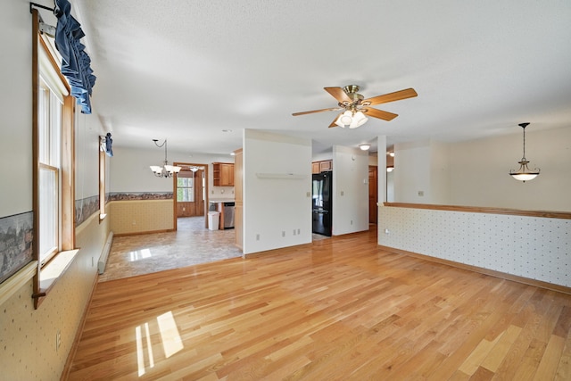 15 Northwood Ct, Wiscasset, ME 04578 - unfurnished living room featuring wallpapered walls, wainscoting, light wood-style floors, a chandelier, and a ceiling fan