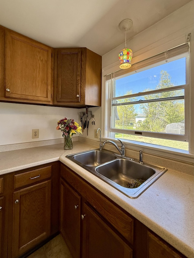 kitchen with a sink, light countertops, pendant lighting, and brown cabinetry
