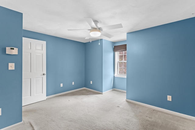 carpeted spare room with a ceiling fan and baseboards