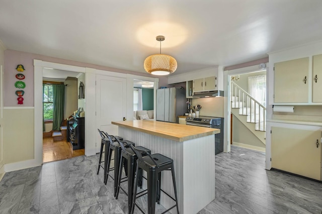 148 Water St, Randolph, ME 04346 - kitchen featuring freestanding refrigerator, under cabinet range hood, a kitchen bar, baseboards, and a kitchen island