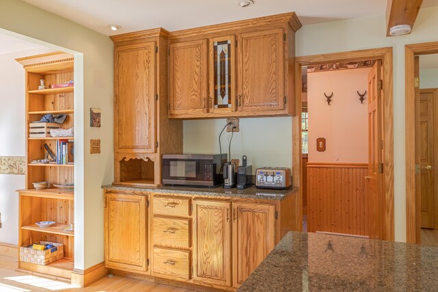 139 Havey Point Rd, Hancock, ME 04640 - kitchen featuring stainless steel microwave, dark stone countertops, glass insert cabinets, wainscoting, and brown cabinetry