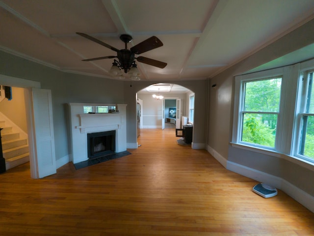 unfurnished living room featuring arched walkways, ceiling fan, baseboards, light wood-style flooring, and ornamental molding