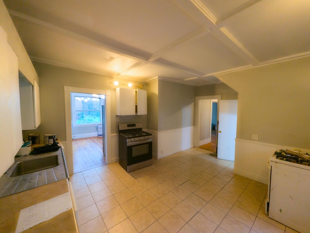 kitchen featuring stainless steel range with gas cooktop, white cabinets, a sink, white gas range oven, and wainscoting