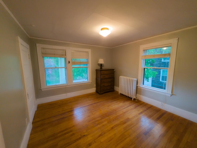 unfurnished room with radiator, wood finished floors, healthy amount of natural light, baseboards, and crown molding
