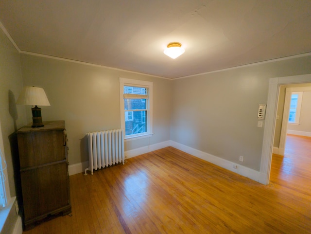 spare room with radiator, wood finished floors, crown molding, and baseboards