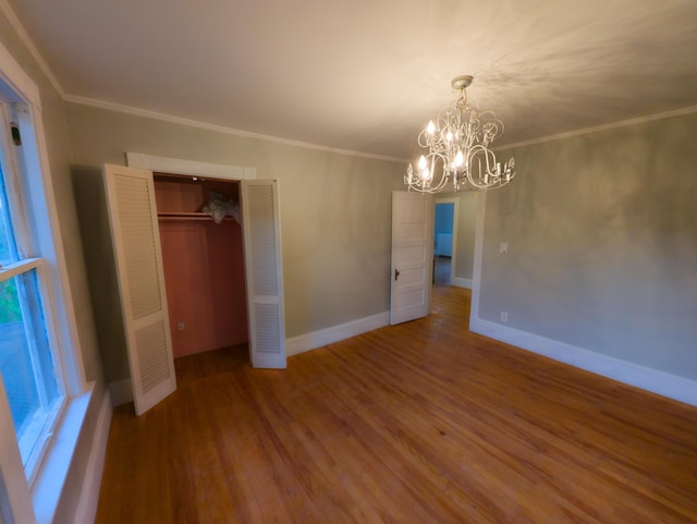unfurnished bedroom featuring a chandelier, wood finished floors, ornamental molding, baseboards, and a heating unit