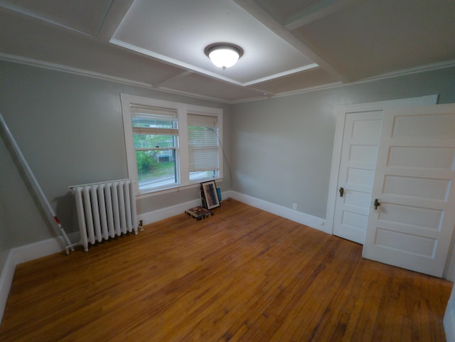 empty room with radiator heating unit, hardwood / wood-style floors, baseboards, and crown molding