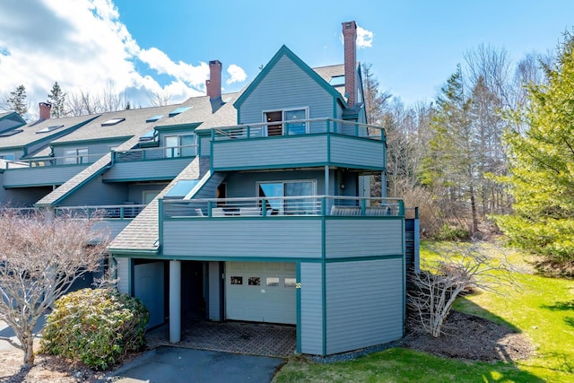 rear view of property featuring a balcony, an attached garage, a chimney, and driveway