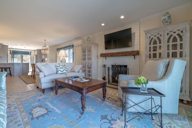 living room with a wall mounted AC, a large fireplace, ornamental molding, wood finished floors, and recessed lighting