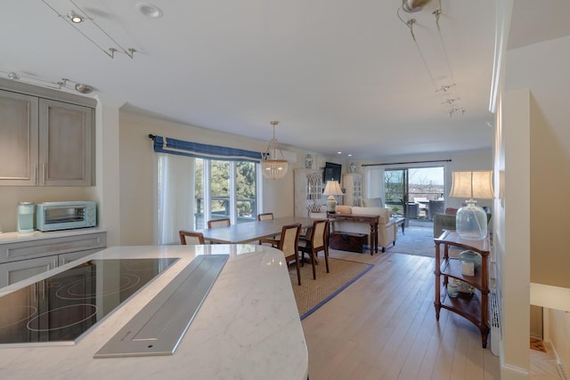 kitchen with black electric stovetop, open floor plan, hanging light fixtures, light stone counters, and light wood-style flooring