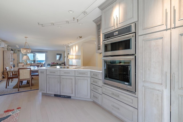kitchen with stainless steel double oven, a peninsula, open floor plan, light wood-style flooring, and light countertops