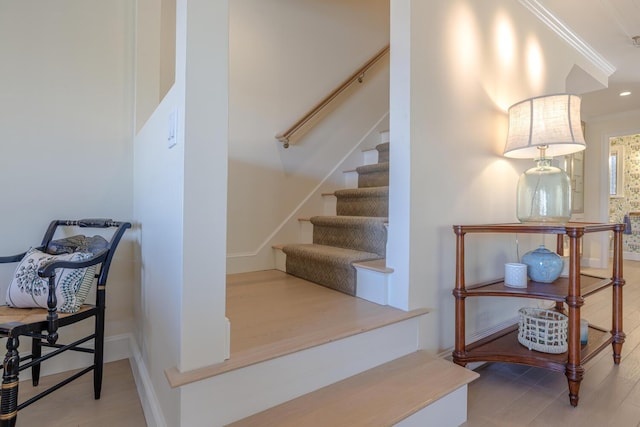 stairs with ornamental molding, wood finished floors, and baseboards