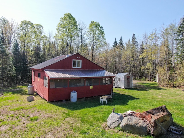 view of property exterior featuring a yard, an outdoor structure, metal roof, a forest view, and a shed