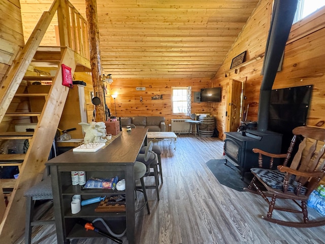 living area featuring vaulted ceiling, a wood stove, wood finished floors, wood walls, and wooden ceiling
