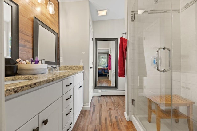 107 Elm St, South Portland, ME 04106 - ensuite bathroom featuring a baseboard heating unit, double vanity, wood finished floors, a shower stall, and baseboards