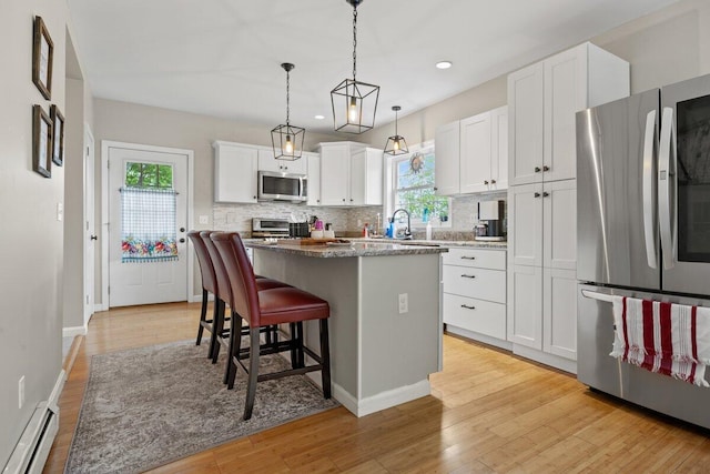 107 Elm St, South Portland, ME 04106 - kitchen with appliances with stainless steel finishes, baseboard heating, a center island, tasteful backsplash, and light wood finished floors