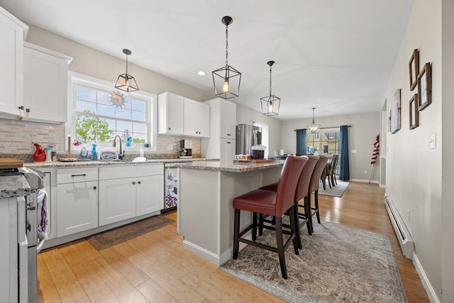 107 Elm St, South Portland, ME 04106 - kitchen with a baseboard heating unit, decorative backsplash, stainless steel appliances, white cabinetry, and recessed lighting
