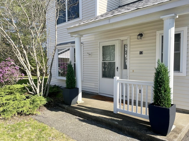 property entrance featuring covered porch and a shingled roof
