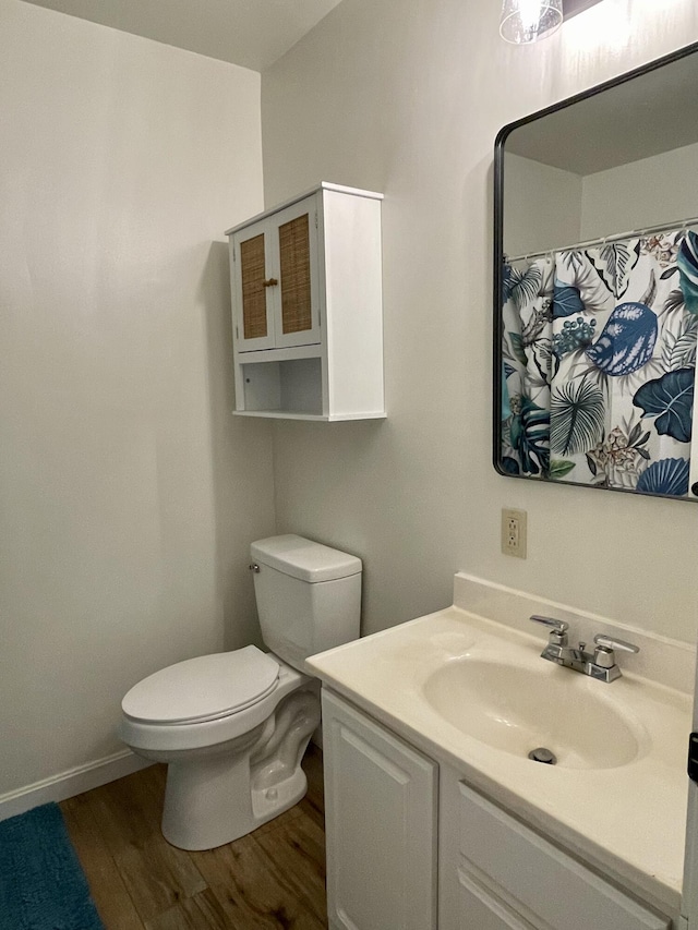 bathroom with wood finished floors, toilet, vanity, and baseboards