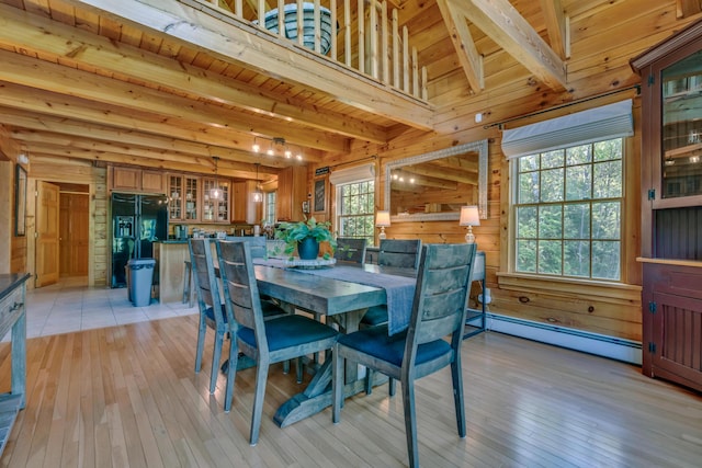 dining room with beamed ceiling, light wood finished floors, a baseboard radiator, wooden ceiling, and wooden walls