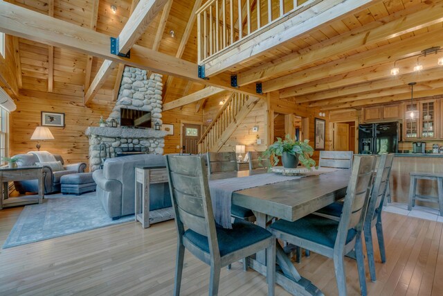 dining space with wood ceiling, beam ceiling, light wood-style flooring, wooden walls, and a stone fireplace