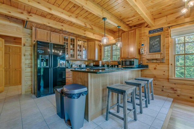 kitchen with black fridge, stainless steel microwave, wood ceiling, wood walls, and healthy amount of natural light
