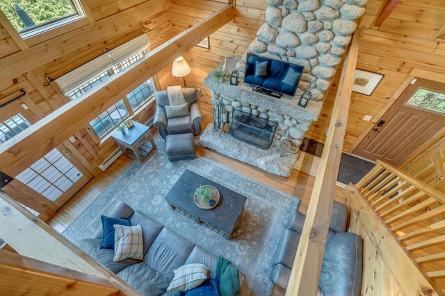 living room featuring a towering ceiling, wooden walls, a fireplace with raised hearth, and wood finished floors