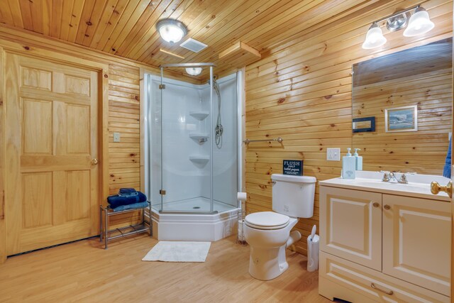 bathroom featuring a shower stall, toilet, wood finished floors, wooden walls, and vanity