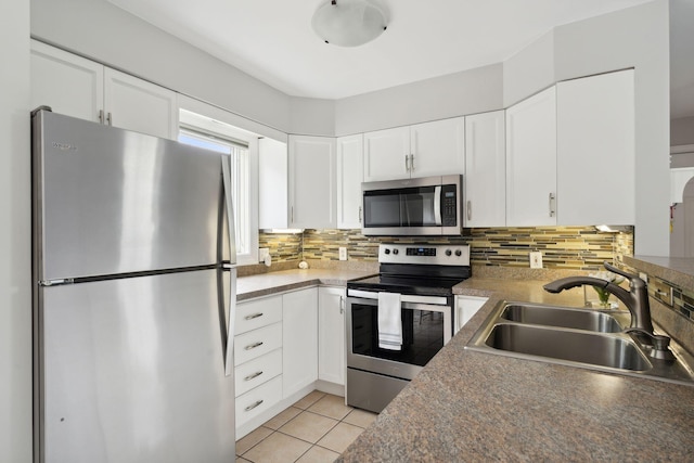 kitchen featuring appliances with stainless steel finishes, a sink, tasteful backsplash, light tile patterned floors, and white cabinets