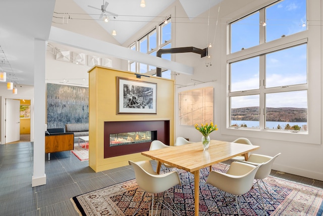 39 Kendall Farm Trl, Rangeley, ME 04970 - dining room featuring a ceiling fan, a glass covered fireplace, a towering ceiling, and a water view