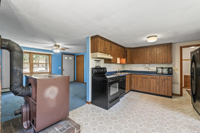 kitchen featuring black appliances, under cabinet range hood, brown cabinetry, dark countertops, and a sink