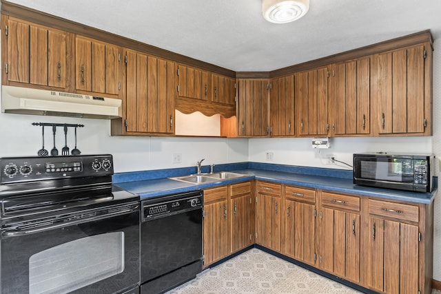kitchen featuring under cabinet range hood, black appliances, a sink, dark countertops, and brown cabinetry
