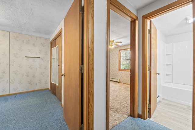 hall featuring a baseboard radiator, carpet flooring, a textured ceiling, wallpapered walls, and baseboards
