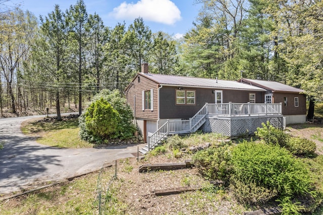 view of front of property featuring stairs, driveway, a chimney, an attached garage, and a wooden deck