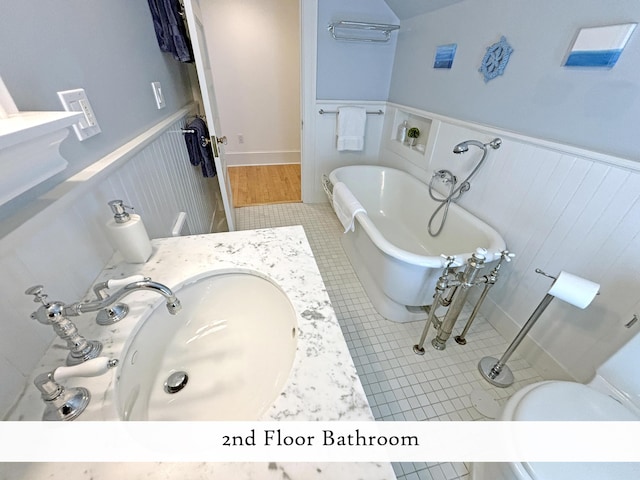 full bath featuring a wainscoted wall, a soaking tub, a sink, tile patterned flooring, and toilet