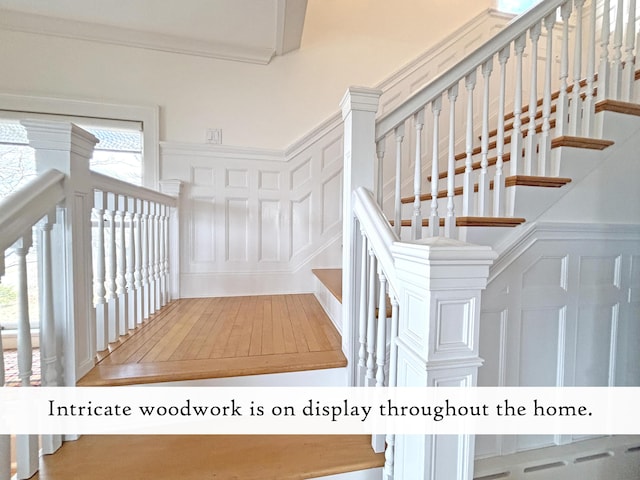 stairway featuring a decorative wall, a wainscoted wall, wood-type flooring, and crown molding