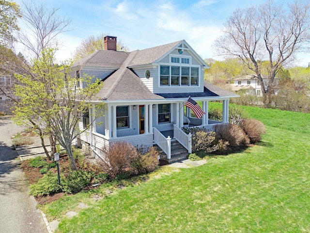 shingle-style home featuring a shingled roof, a front lawn, covered porch, and a chimney