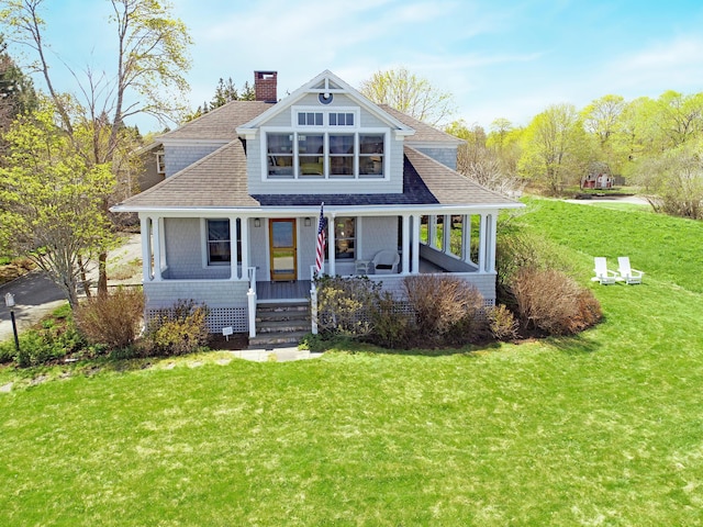 shingle-style home featuring a front lawn, a chimney, roof with shingles, and a porch