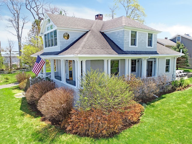 shingle-style home with roof with shingles, a front lawn, and a chimney