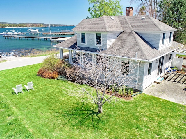 back of property featuring a chimney, a water view, a shingled roof, a yard, and a patio area