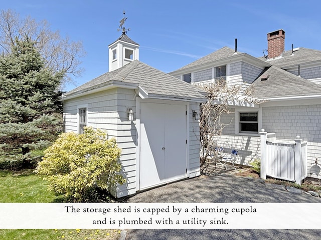 back of house featuring a storage shed, an outdoor structure, roof with shingles, and a chimney