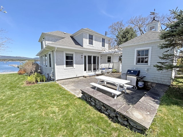 back of property with a pergola, a lawn, a water view, a patio, and roof with shingles