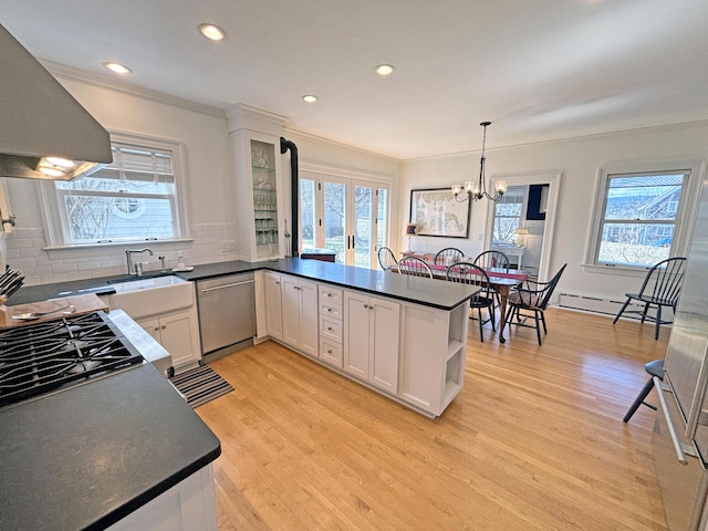 kitchen with dishwasher, wall chimney exhaust hood, dark countertops, tasteful backsplash, and light wood-type flooring
