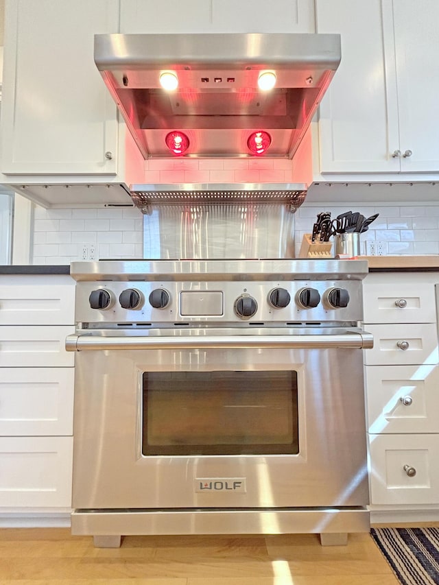 kitchen view of ventilation hood, premium range, backsplash, and white cabinetry