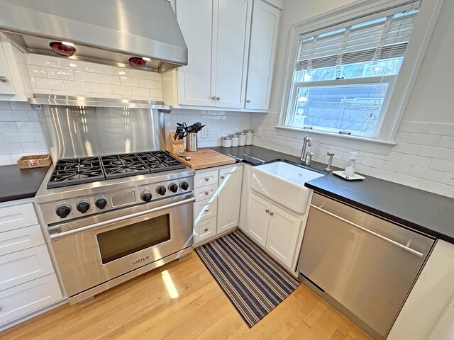 kitchen with stainless steel appliances, exhaust hood, light wood-type flooring, and dark countertops